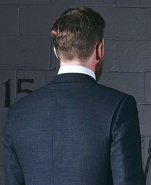 Product shot rear view of the Action Back Bi-Swing Back on a blue birdseye suit worn by a model in a shooting range